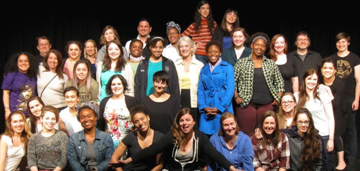 A large group of artists of different ethnicities and genders in contemporary casual dress gather on a stage, smiling at the camera